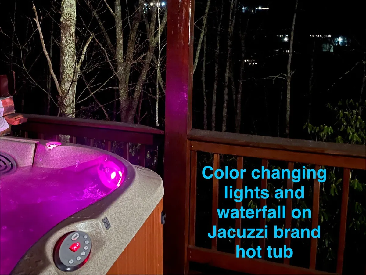 A luxurious outdoor Jacuzzi hot tub with color-changing lights and a waterfall feature, nestled among trees. The scene is set for serene relaxation or socializing under the stars, emphasizing privacy and the connection to the natural surroundings.