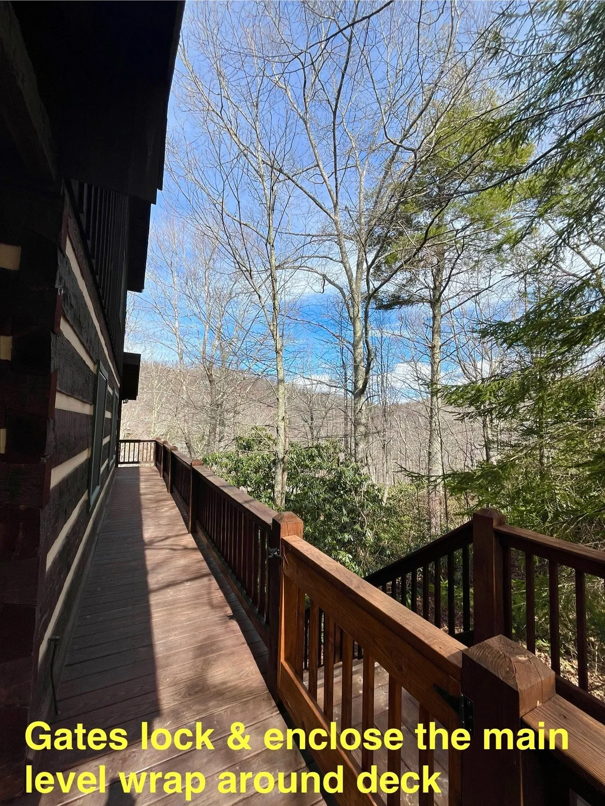 A spacious wrap-around deck with safety gates overlooking mountain scenery and surrounded by trees. The wooden railing and open design create an inviting space for families, with plenty of room for kids or dogs to play safely while adults enjoy the view.