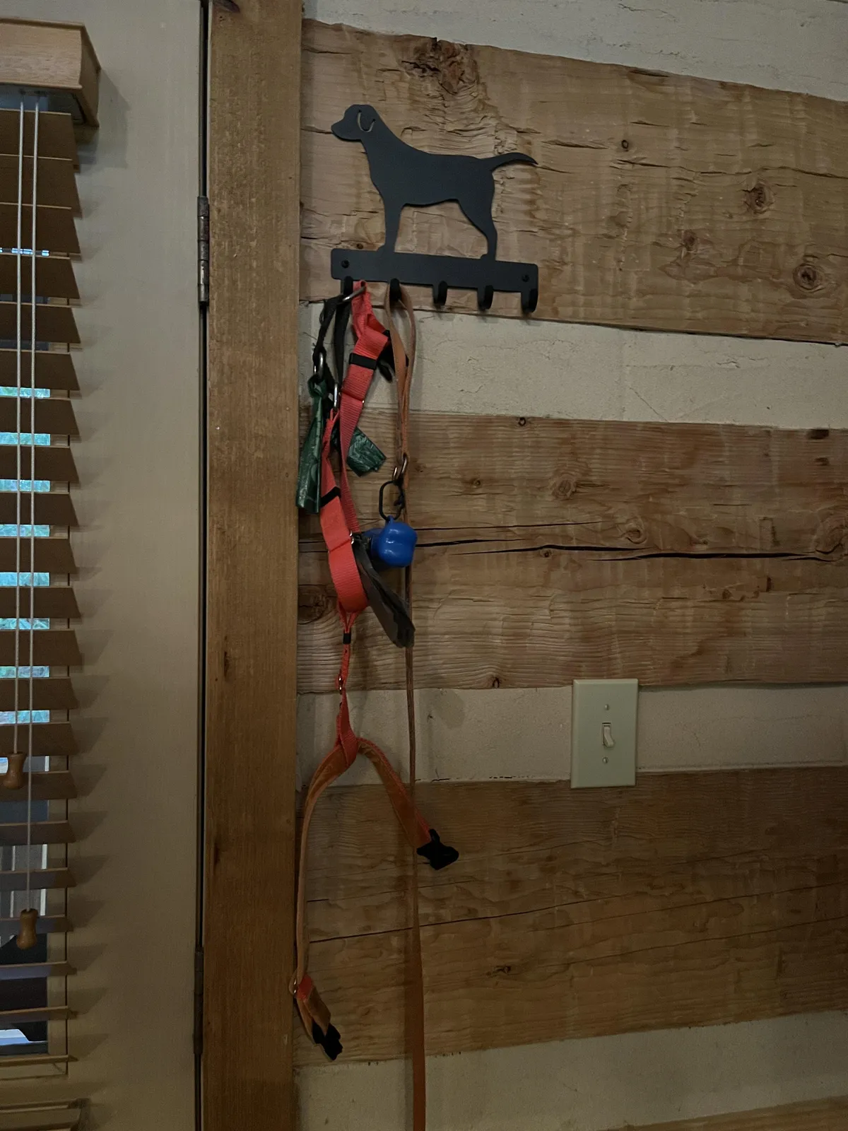 An interior shot focused on a charming dog silhouette hook mounted on a wooden wall, with leashes hanging and a sense of homey warmth. The image evokes the daily routines and special moments shared with a beloved pet.
