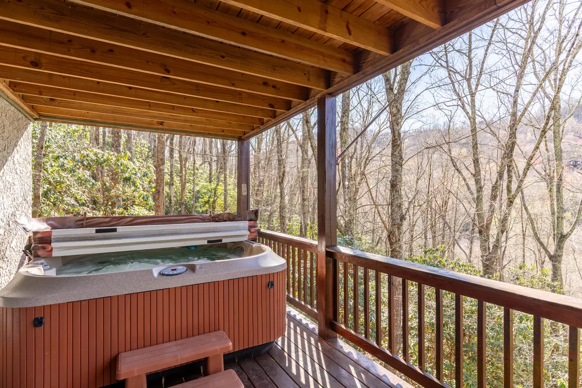 This exterior image features a hot tub on a wooden deck surrounded by lush trees, creating an intimate and serene setting. The view showcases the privacy and natural beauty of the cabin's outdoor amenities, inviting relaxation and romantic stargazing.